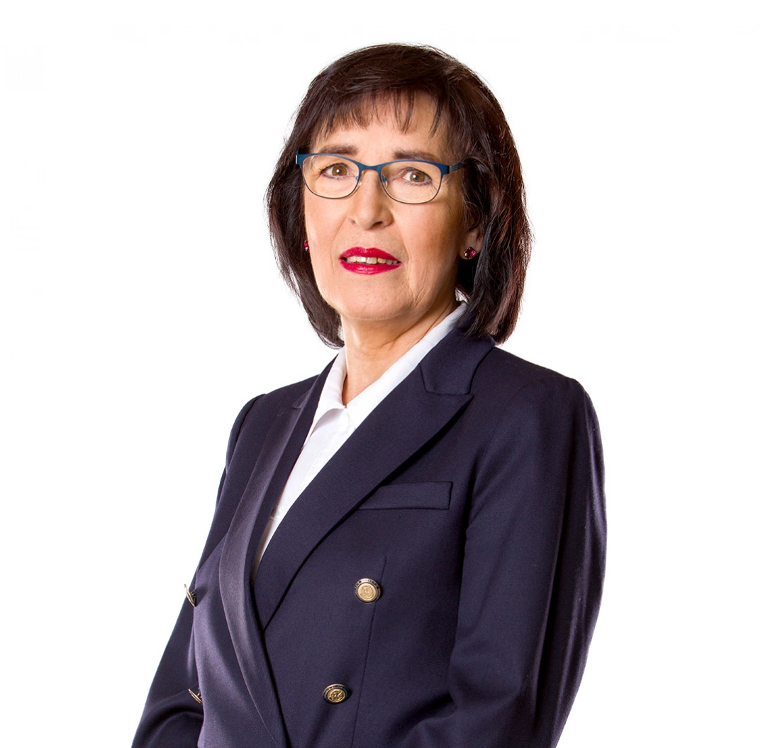 Kobieta w eleganckim garniturze, z okularami i uśmiechem, pozująca na białym tle.