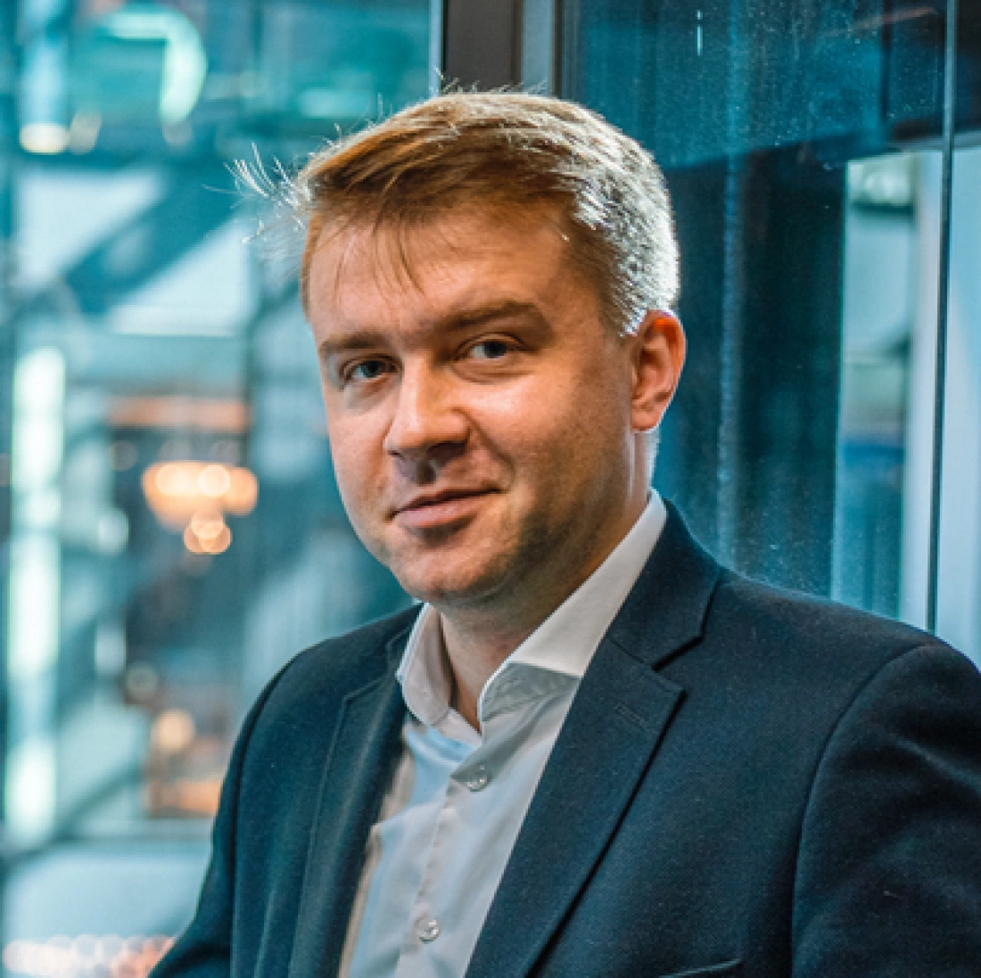 Mężczyzna w garniturze stojący przy szklanej ścianie.