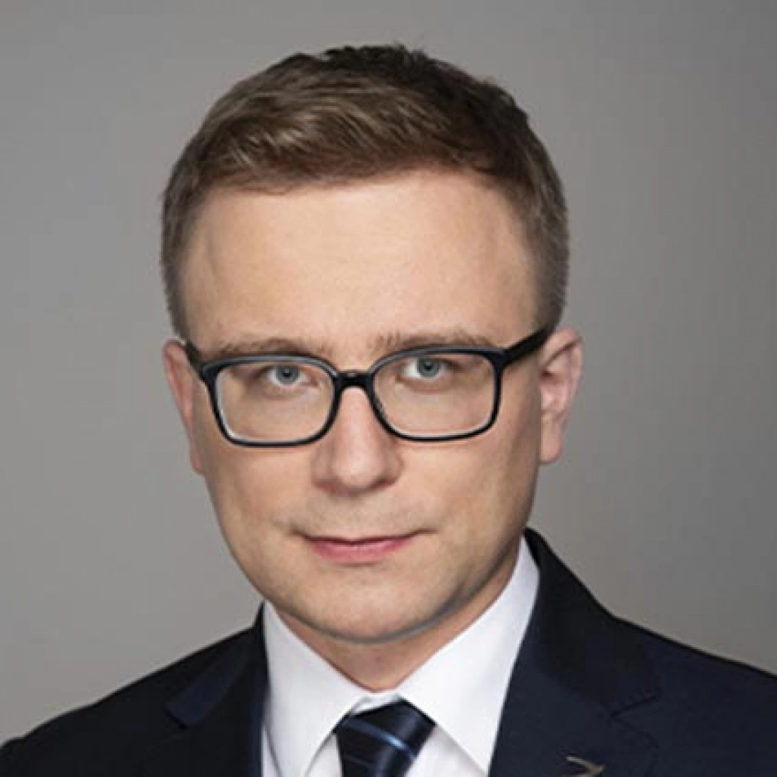 Mężczyzna w okularach, ubrany w garnitur.