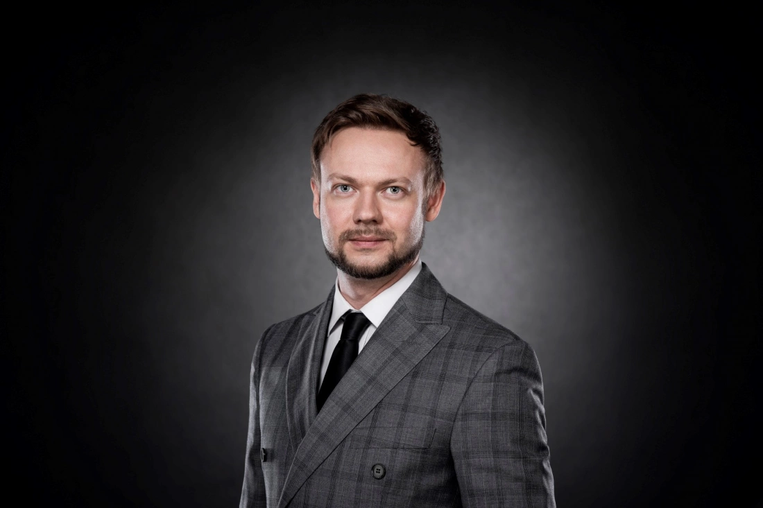 Mężczyzna w eleganckim szarym garniturze na ciemnym tle.