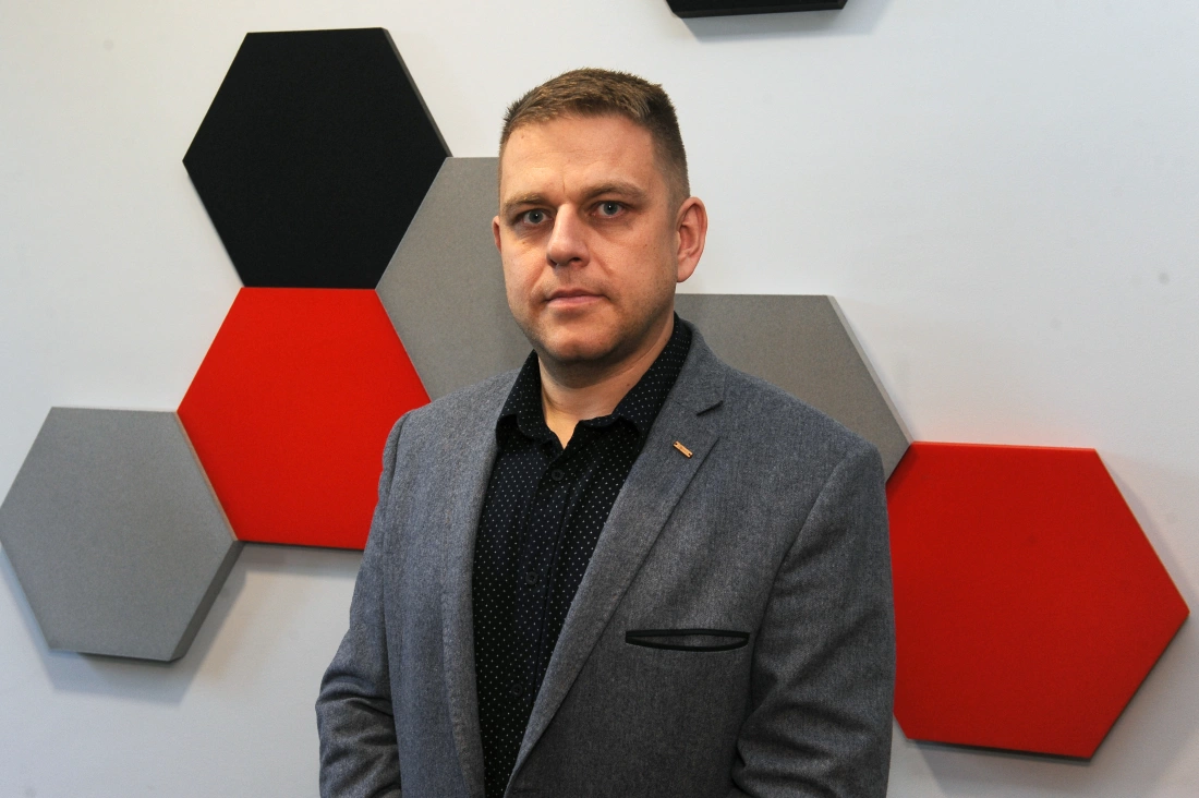 Mężczyzna w eleganckim ubraniu stoi na tle geometrycznych, kolorowych paneli.