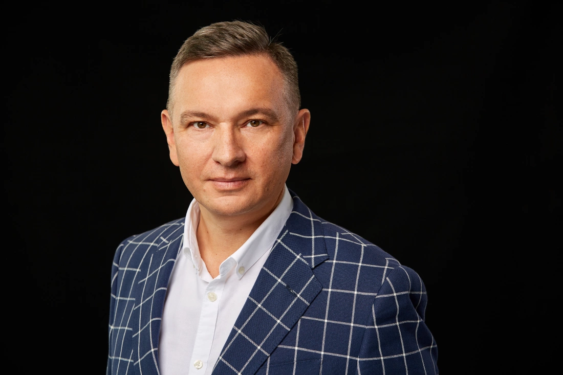 Mężczyzna w niebieskiej marynarce w kratę, na tle czarnym.