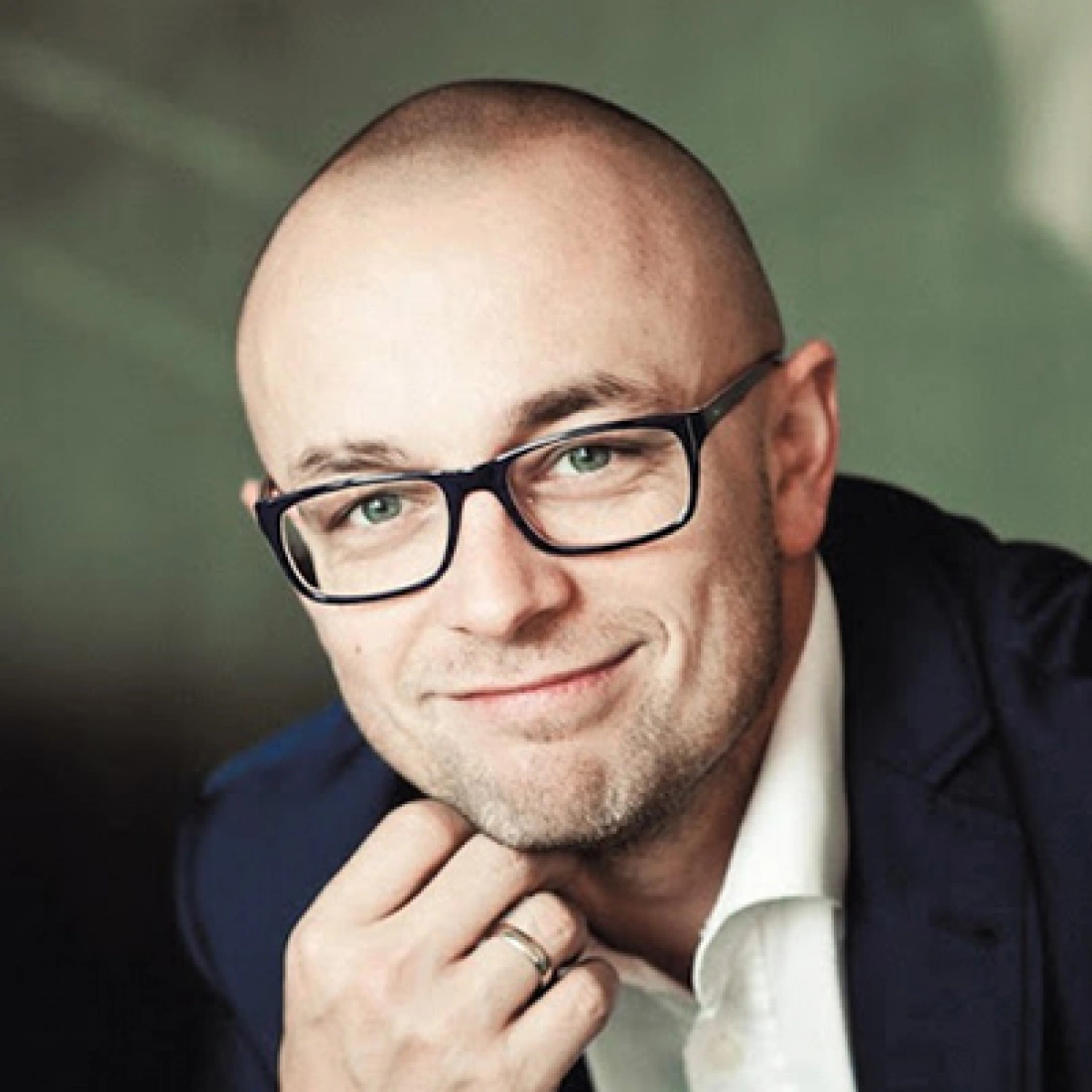 Mężczyzna w okularach, ze szczerym uśmiechem, na neutralnym tle.