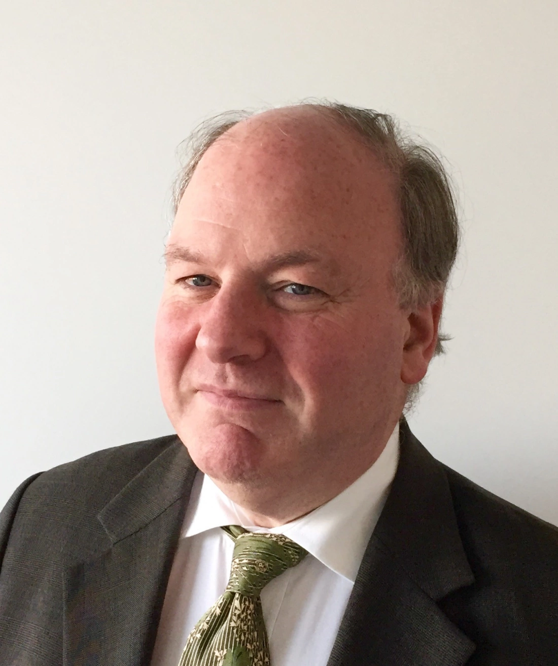 Mężczyzna w garniturze z zielonym krawatem, uśmiechający się podczas pozowania.