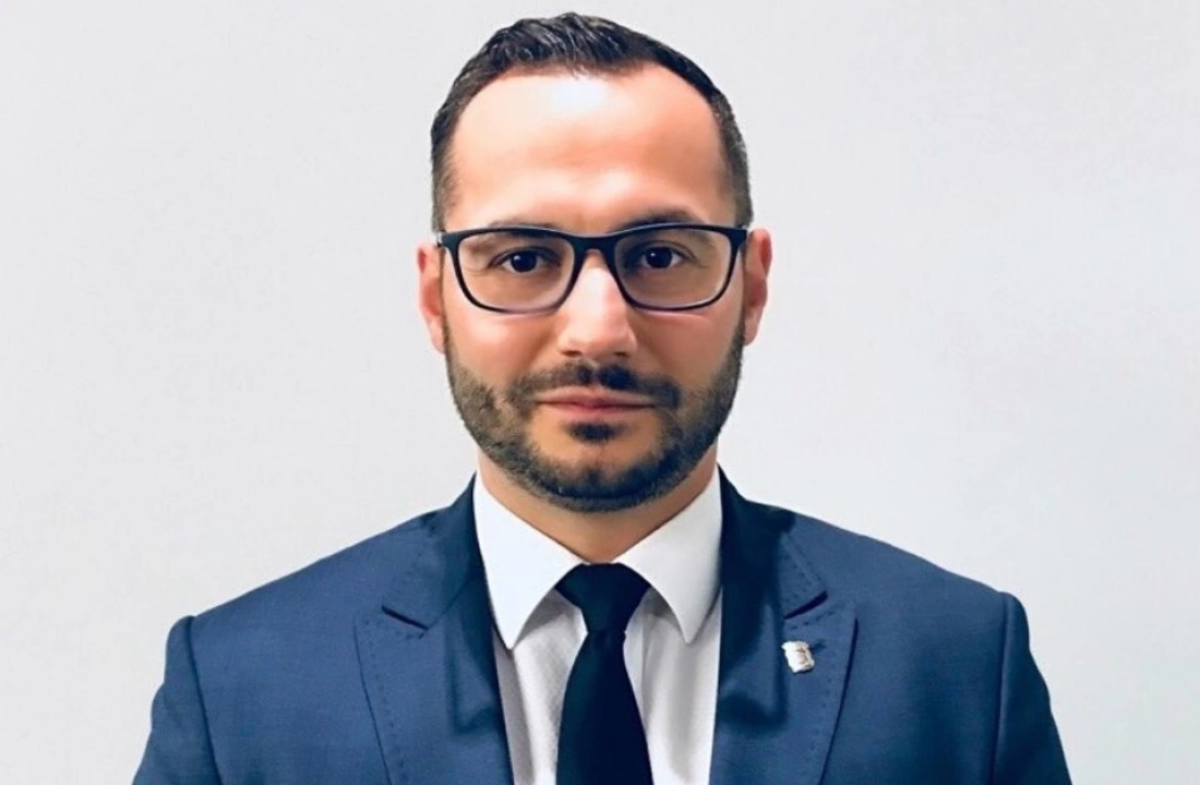 Mężczyzna w garniturze z okularami, patrzy śmiało w stronę kamery.