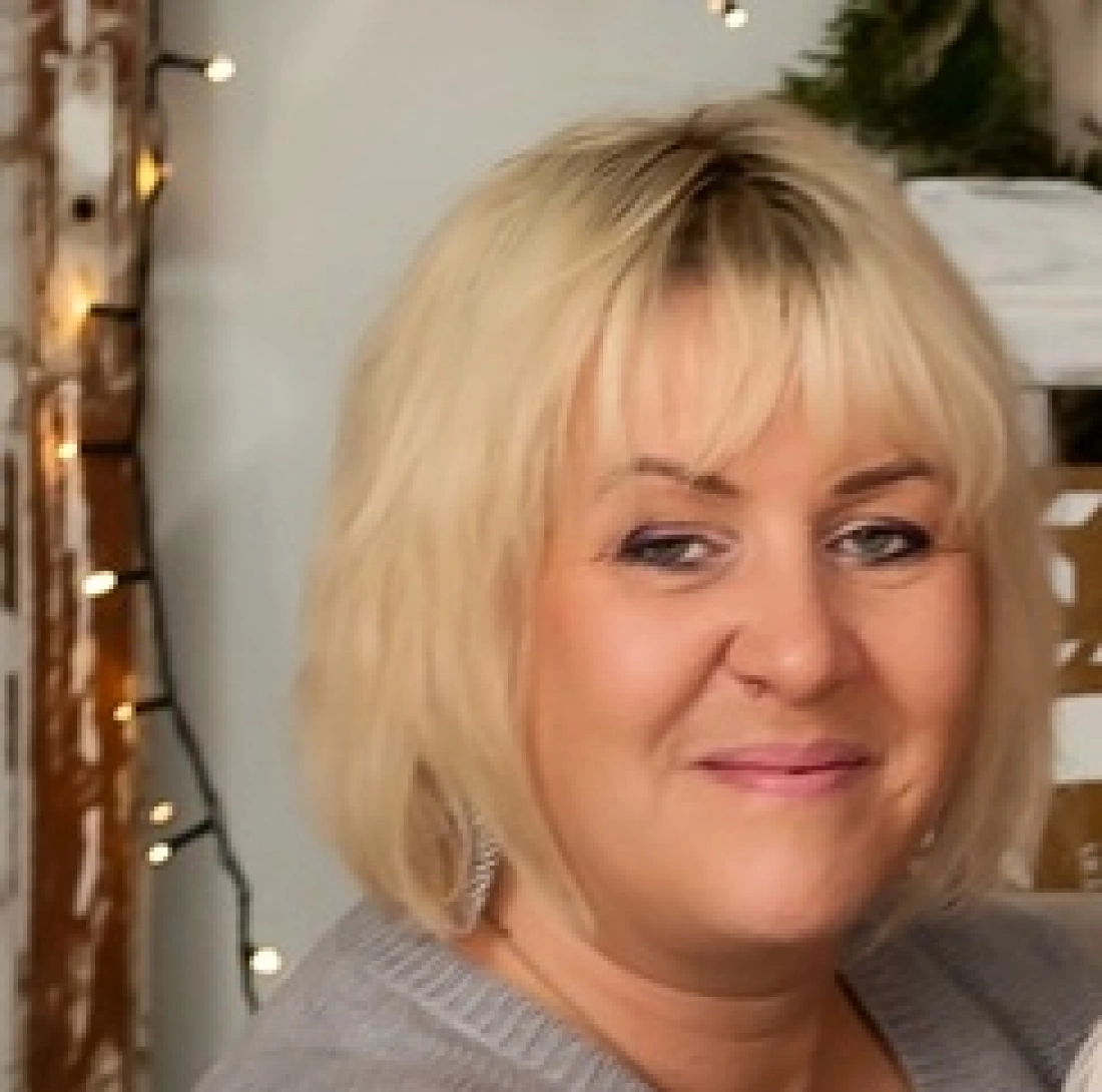 Kobieta w niebieskim płaszczu z mapą, siedząca na kamieniach nad brzegiem morza, z pochmurnym niebem w tle.