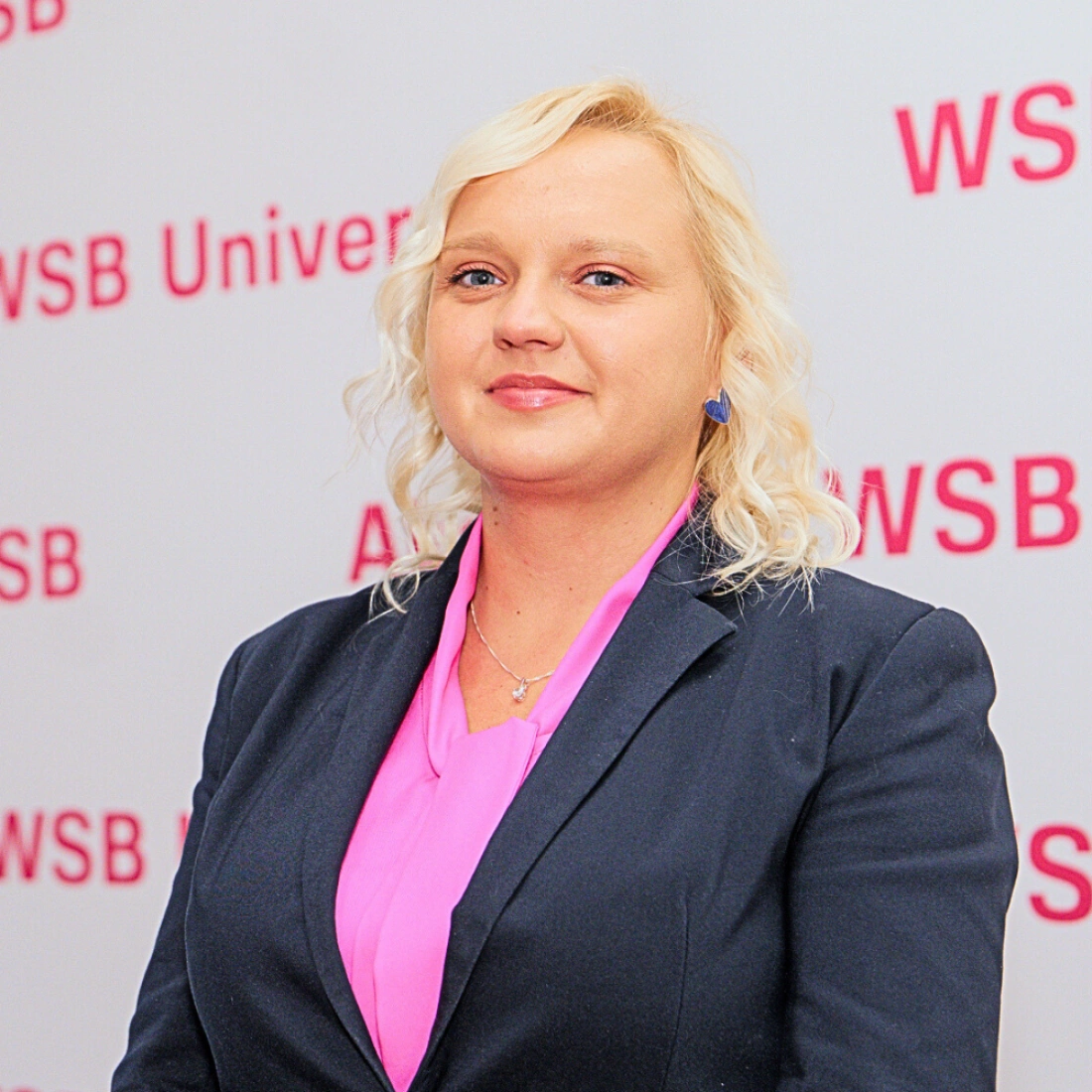 Mężczyzna w niebieskim garniturze z założonymi rękami stoi na stacji kolejowej.