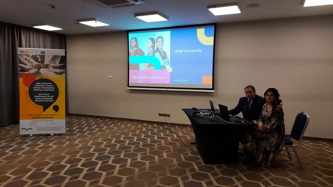 Spotkanie w sali konferencyjnej z prezentacją WSB University i uczestnikami przy stole.