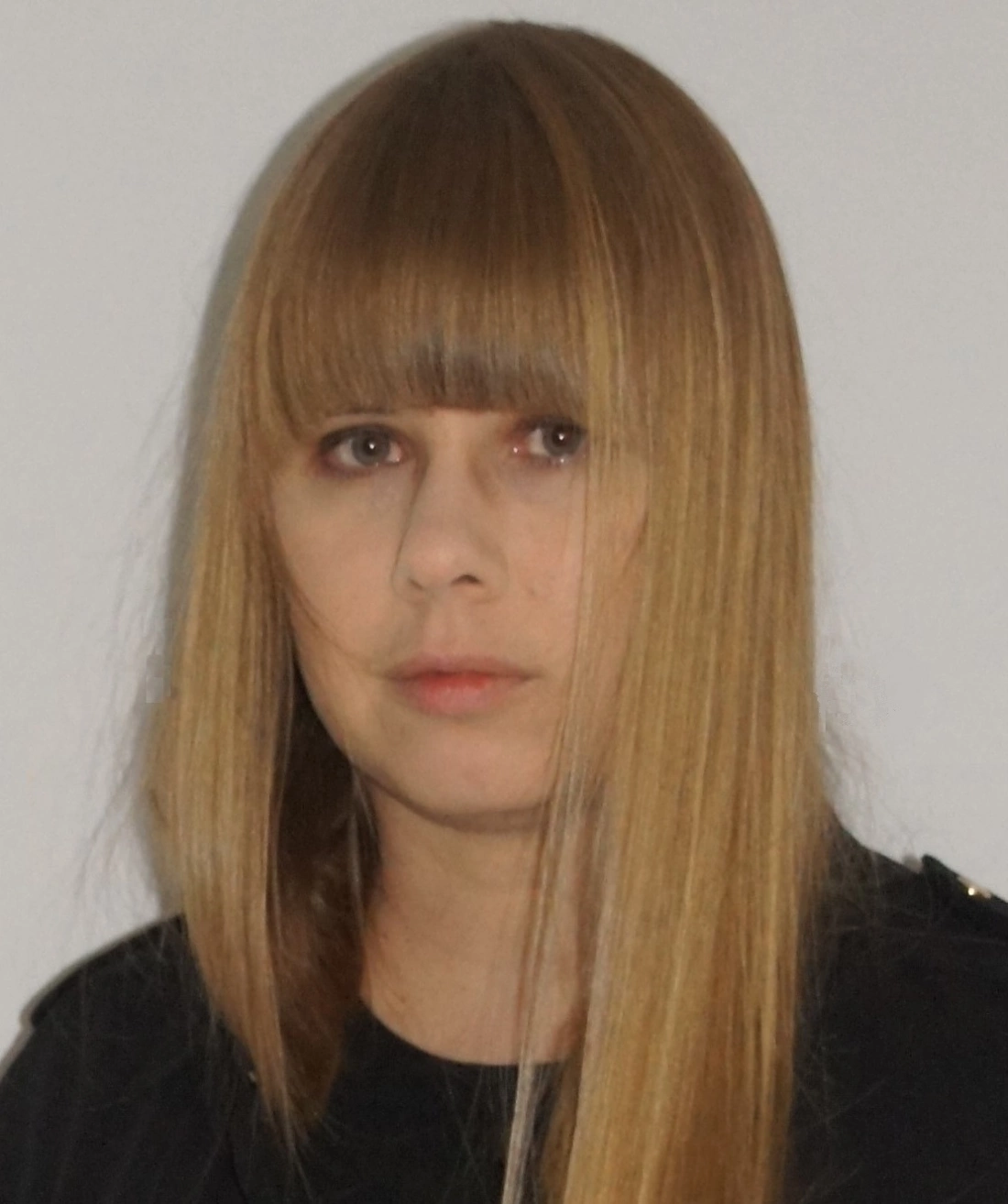 Portret osoby z długimi, prostymi włosami i znakiem skupienia na twarzy.