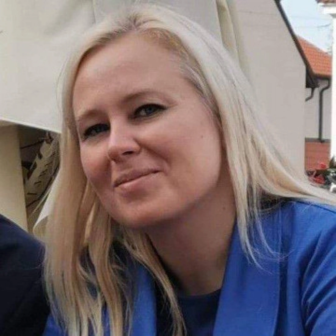 Kobieta z długimi blond włosami, uśmiechająca się w niebieskiej bluzie.