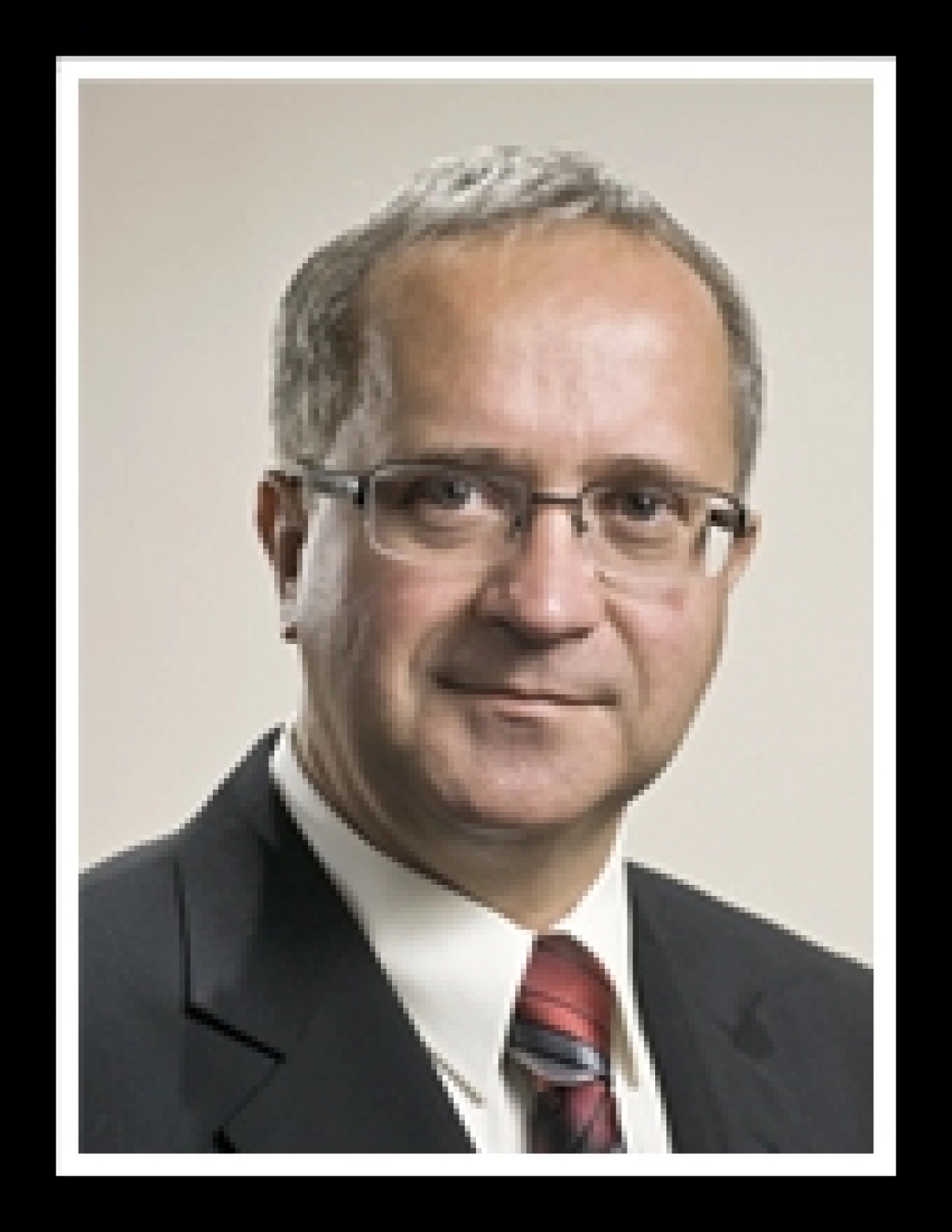 Mężczyzna w garniturze z okularami, patrzący w obiektyw.