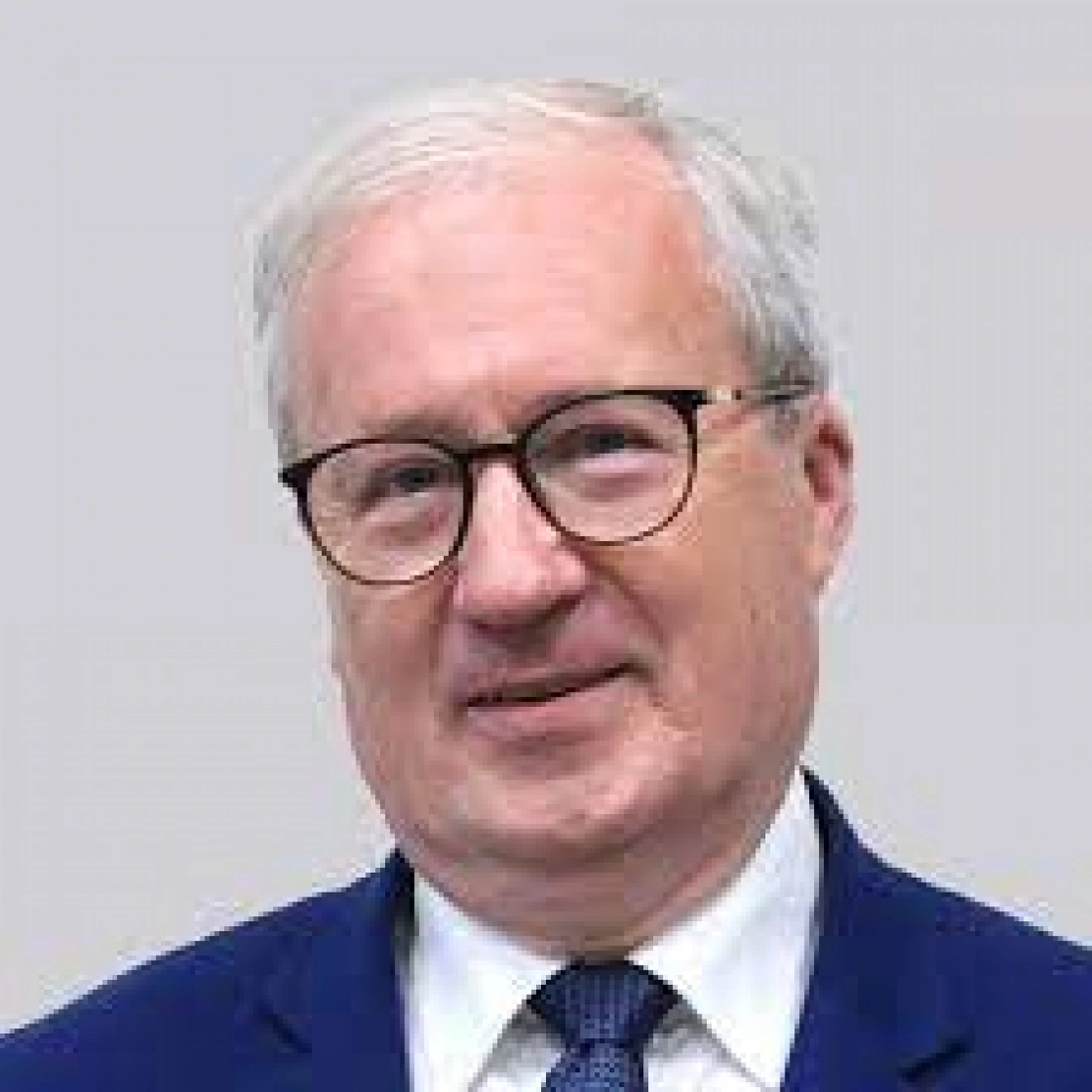 Mężczyzna w okularach, uśmiechający się na szarym tle.