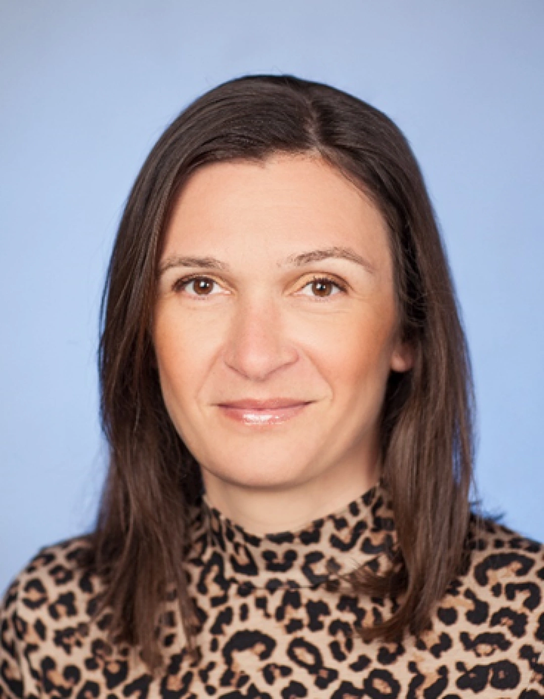 Kobieta z długimi, ciemnymi włosami w bluzce w cętki, na tle niebieskim.