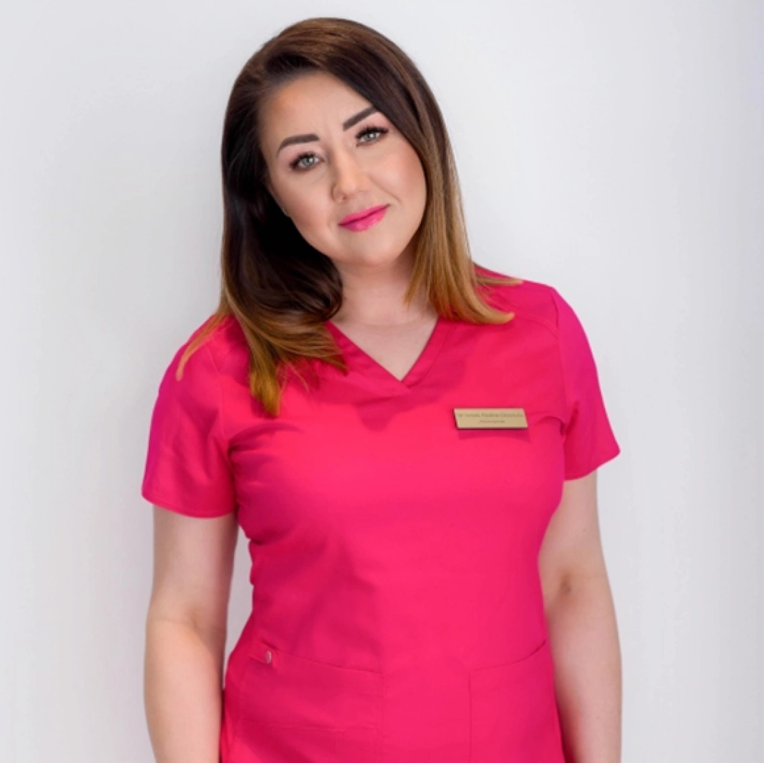 Kobieta w różowej uniformie medycznym, z uśmiechem na twarzy.