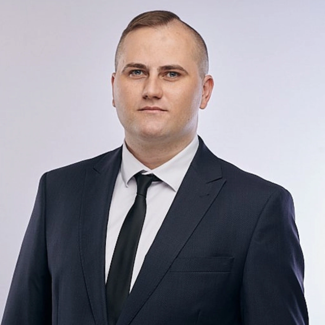 Mężczyzna w garniturze, stojący na jasnym tle.