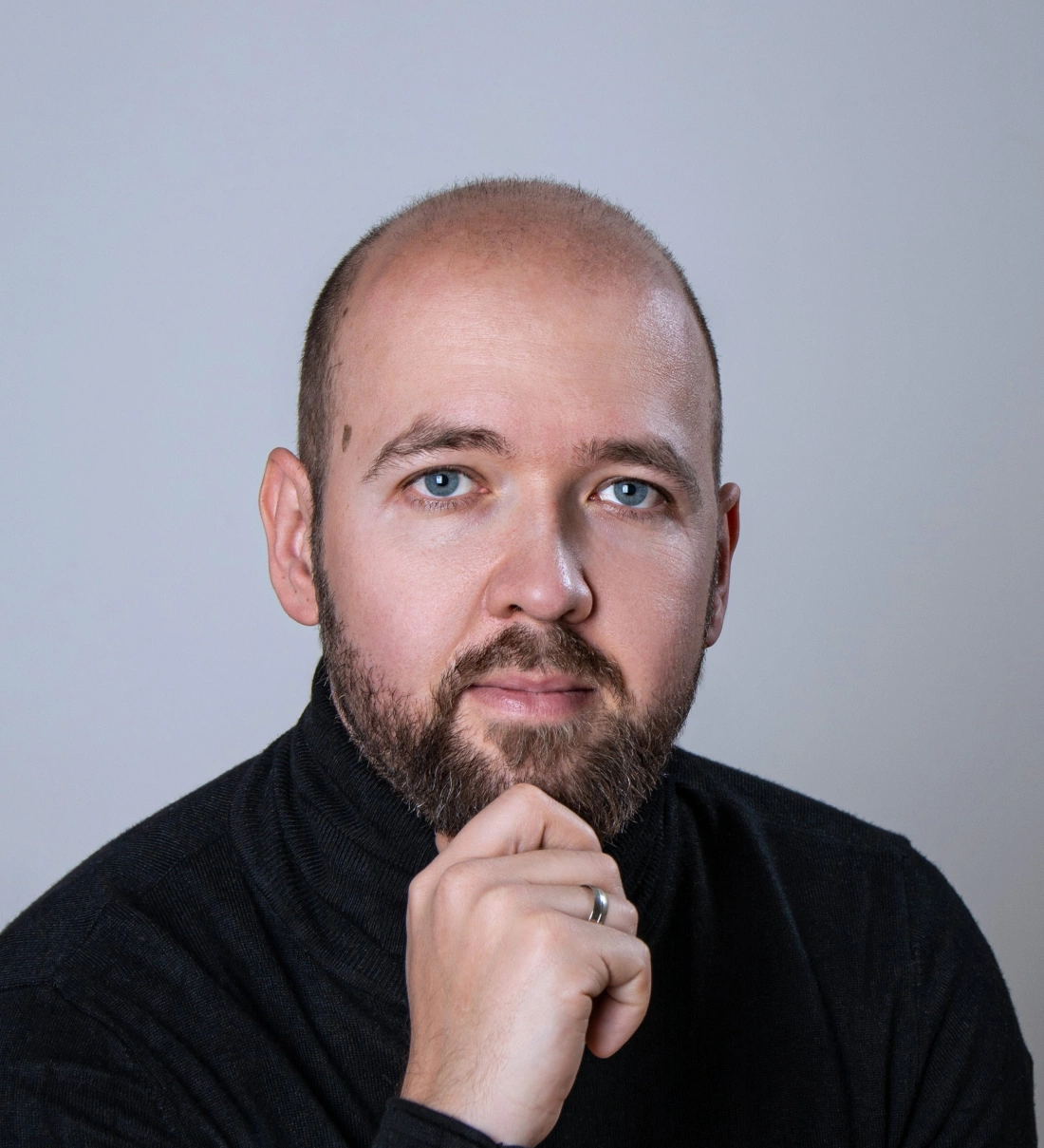 Mężczyzna z brodą w czarnym swetrze, patrzący w obiektyw.
