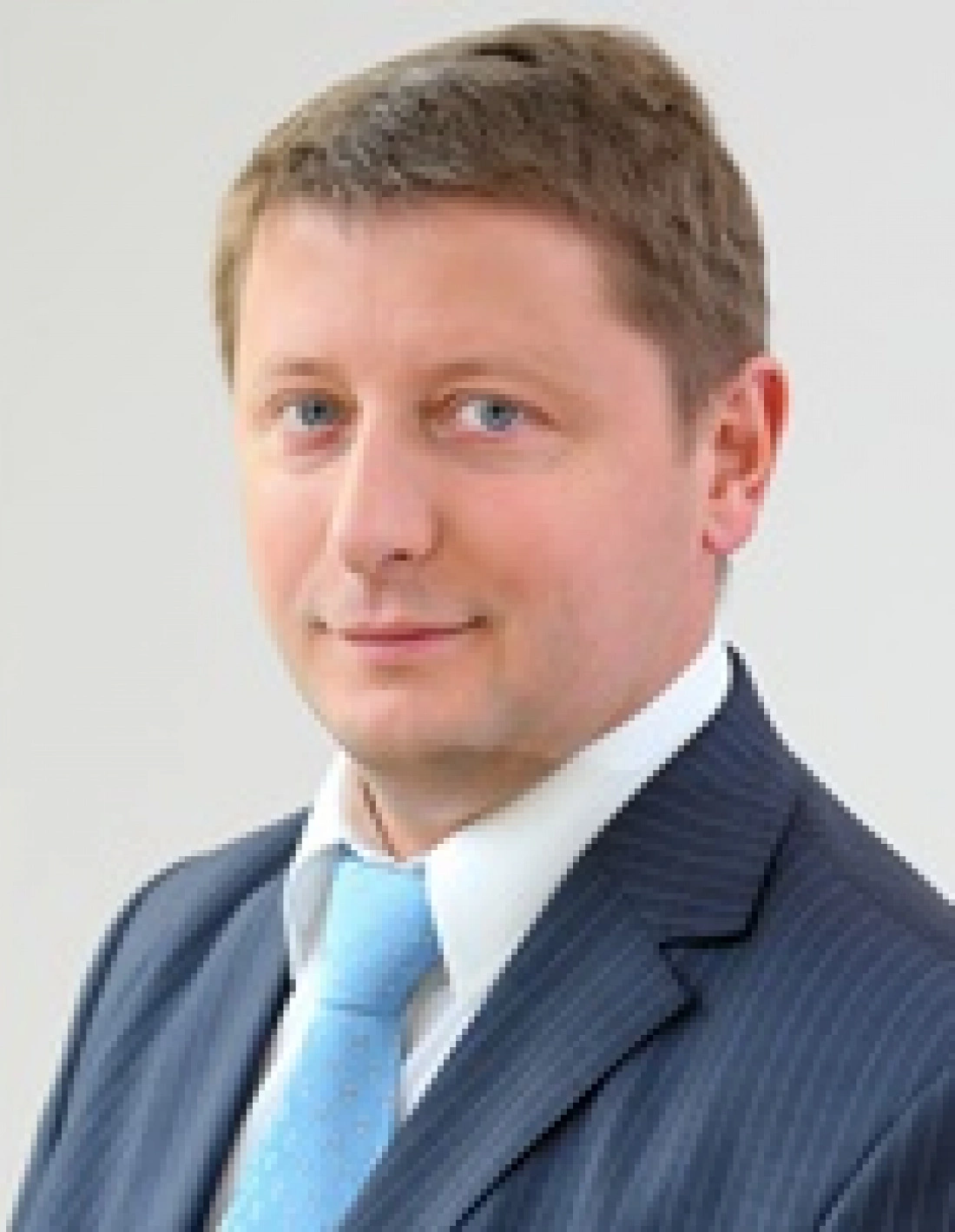 Mężczyzna w garniturze z jasnym krawatem, na neutralnym tle.