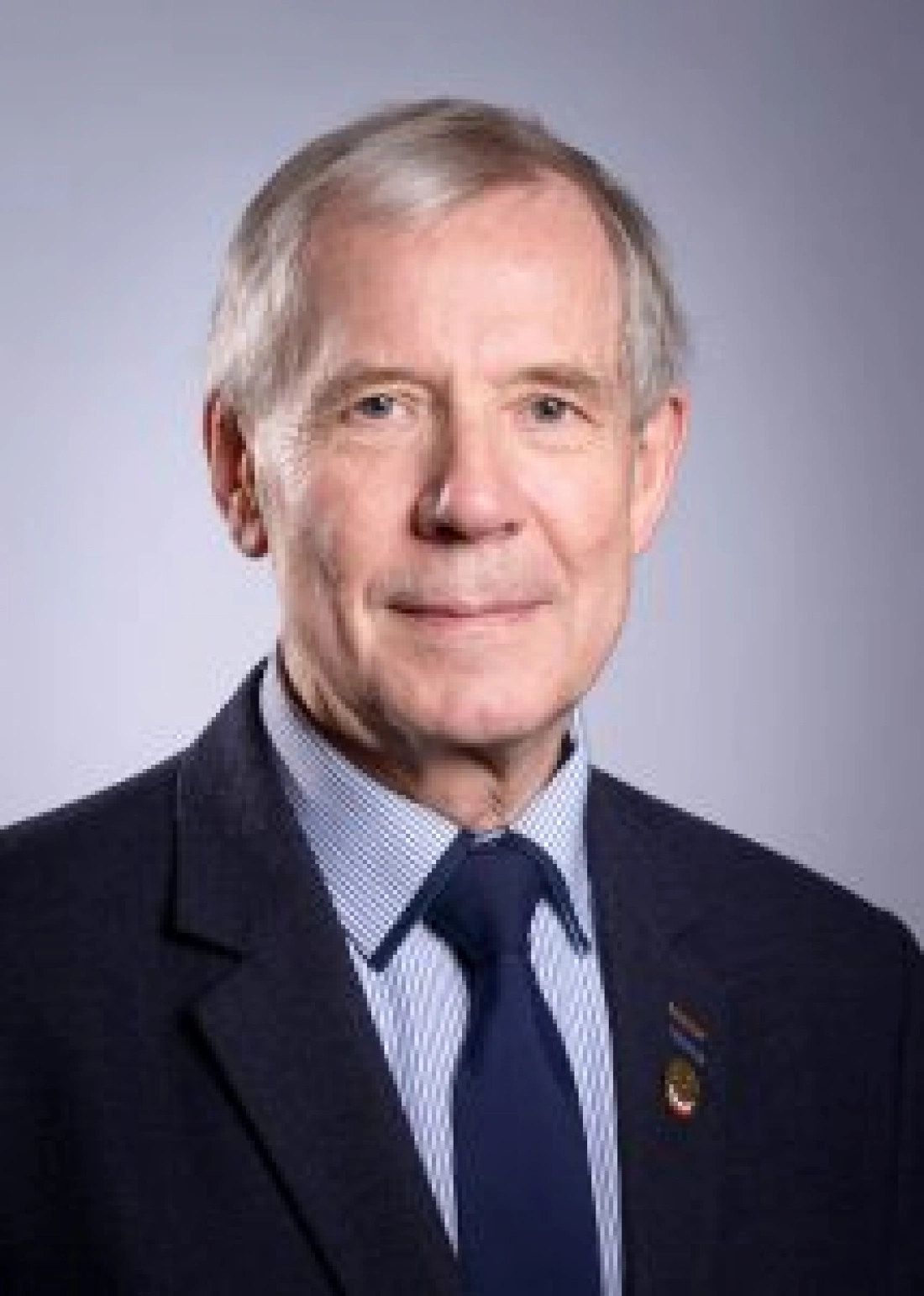 Mężczyzna w średnim wieku, w ciemnym garniturze, z siwymi włosami i krawatem.