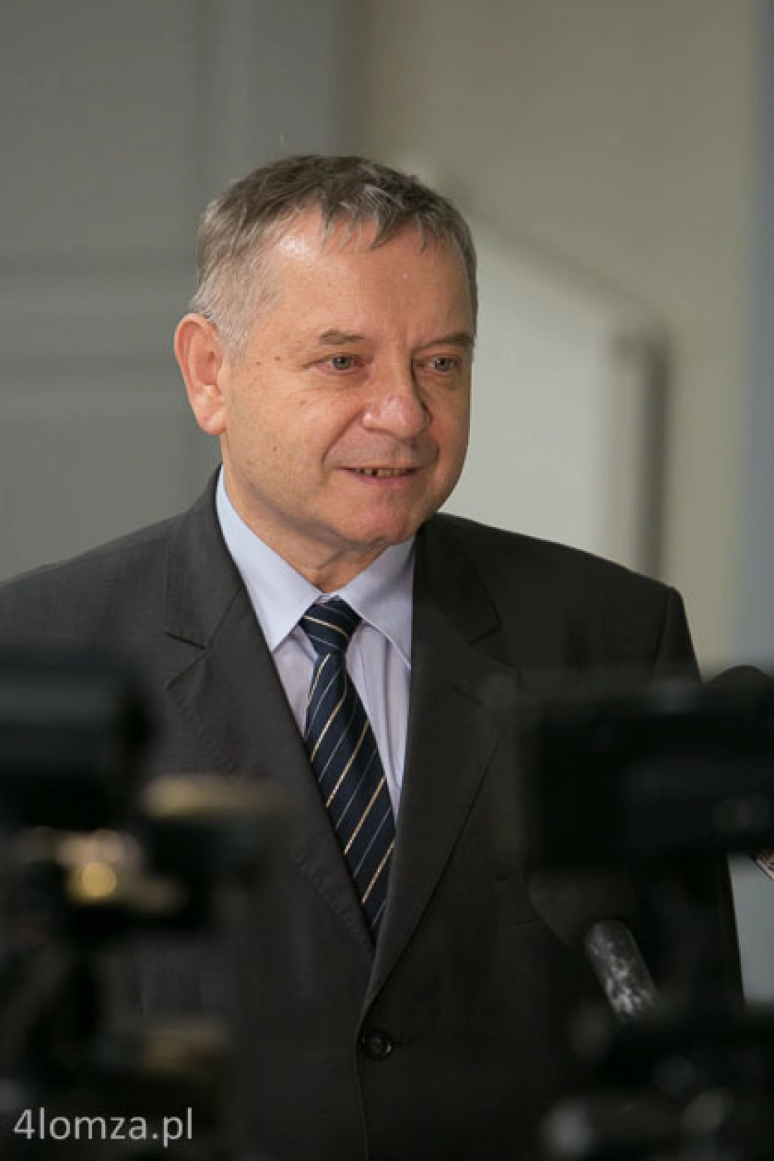 Mężczyzna w garniturze uśmiecha się podczas konferencji prasowej.