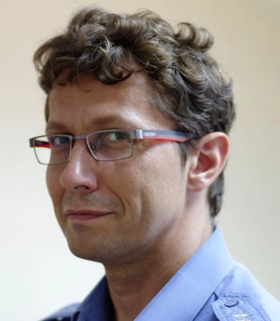 Mężczyzna z okularami, o kręconych włosach, w niebieskiej koszuli.