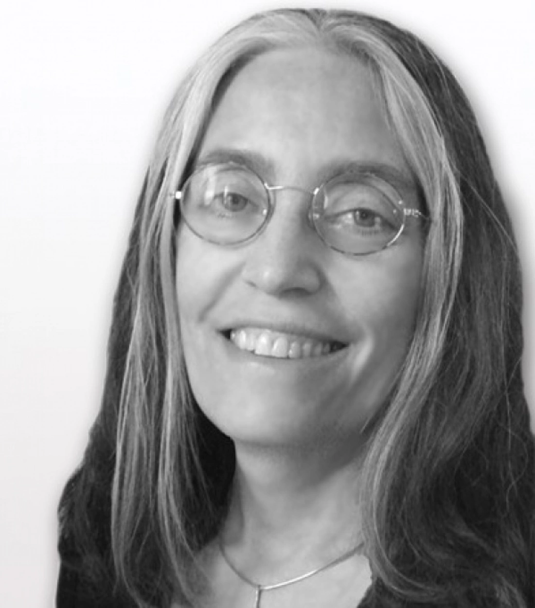 Portret uśmiechniętej kobiety z długimi, siwymi włosami, w okularach.