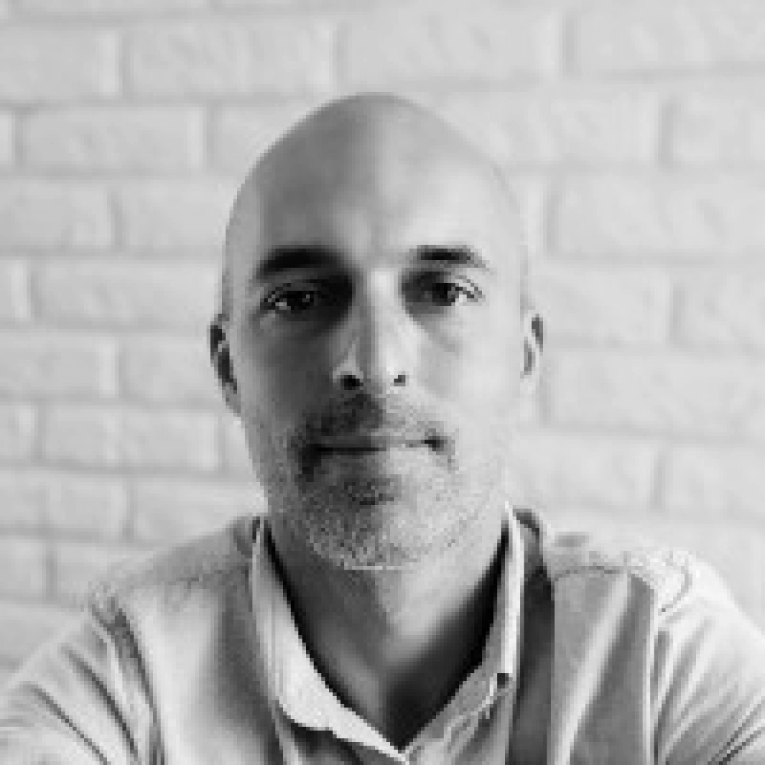 Mężczyzna z krótkimi włosami i zarostem na tle jasnej ściany.