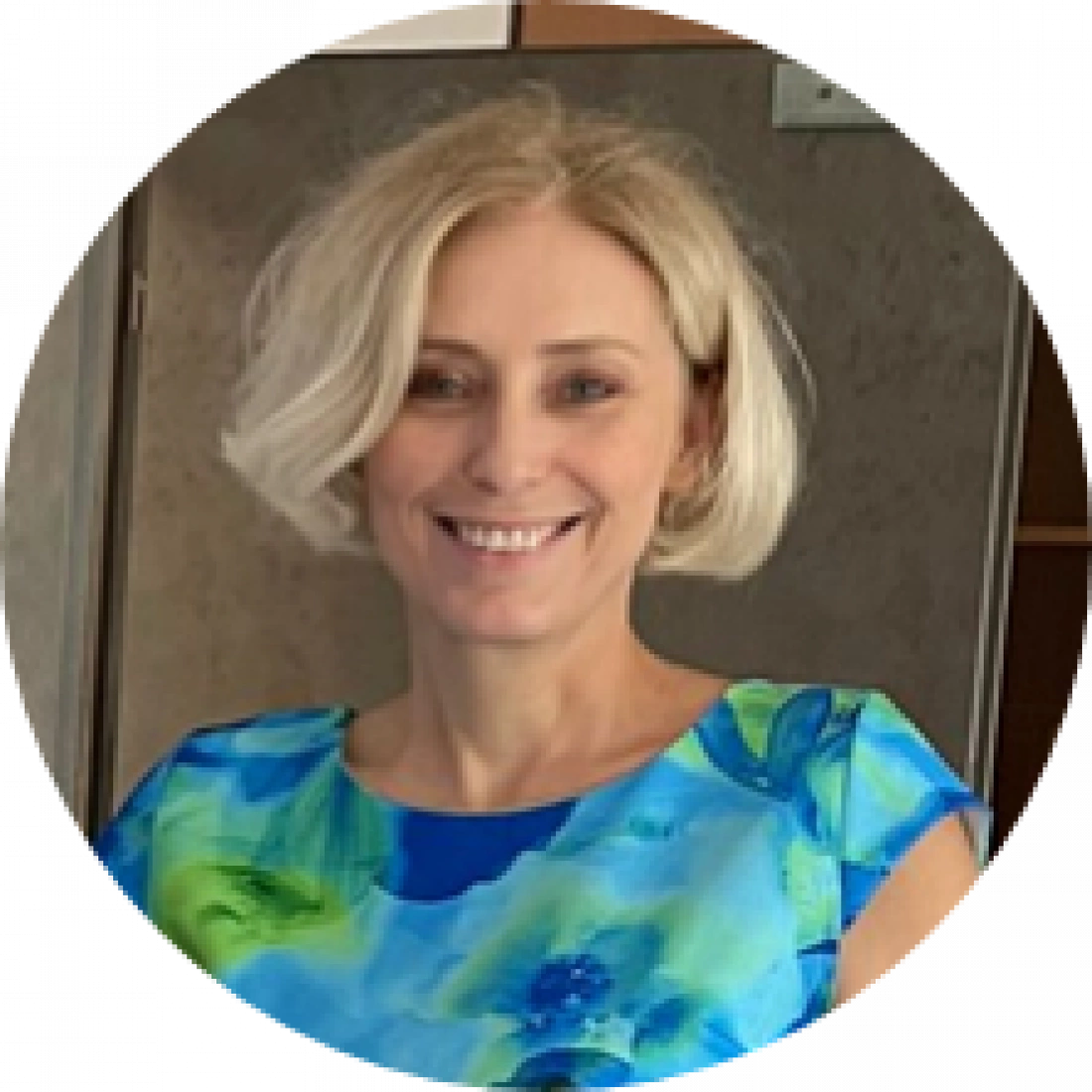 Kobieta z blond włosami, uśmiechająca się i ubrana w kolorową bluzkę.