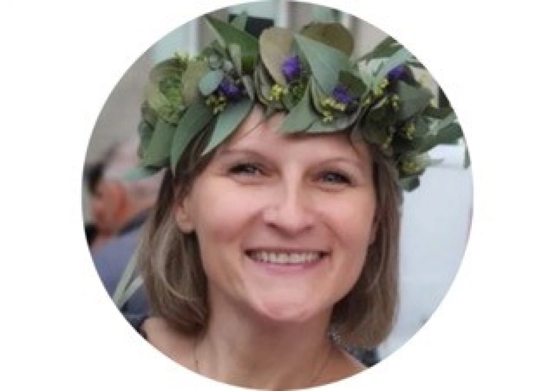 Kobieta z uśmiechem, nosząca wieniec z liści i kwiatów.