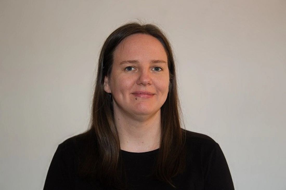 Kobieta o długich ciemnych włosach, uśmiechająca się na neutralnym tle.