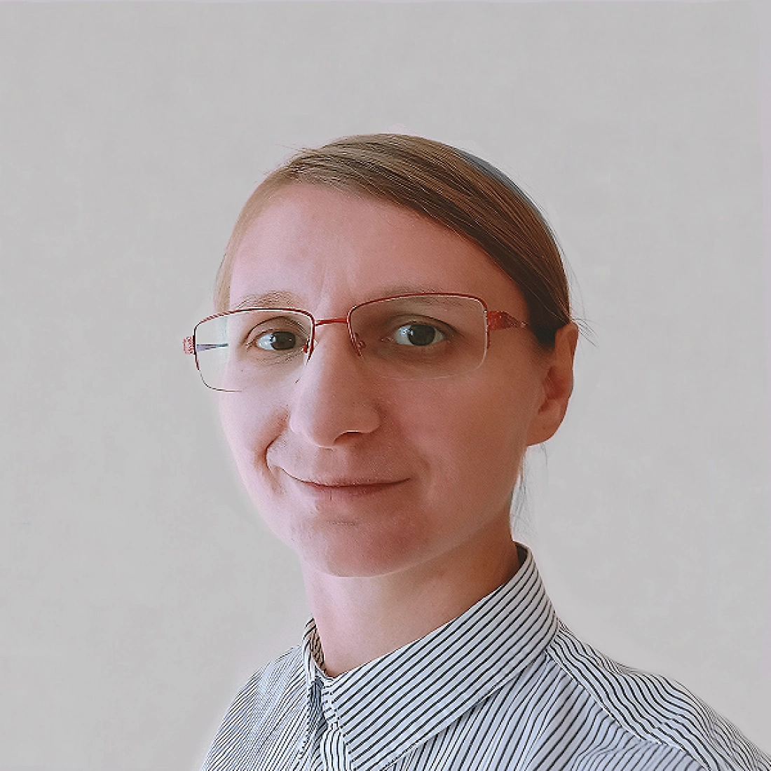 Kobieta w okularach, uśmiechająca się, w koszuli w paski na tle w jasnym kolorze.