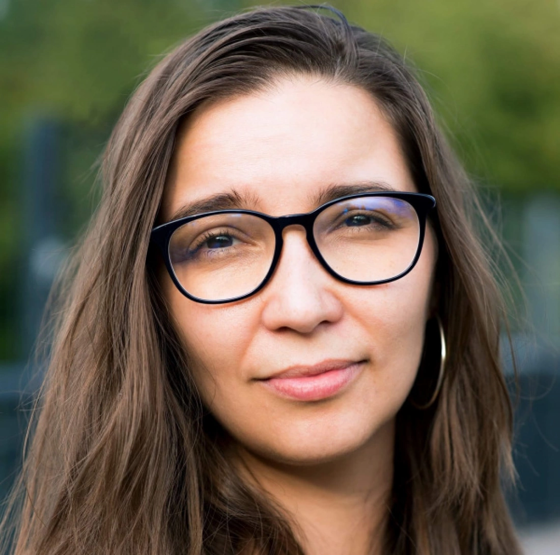 Kobieta z długimi włosami i okularami, patrząca prosto w obiektyw.