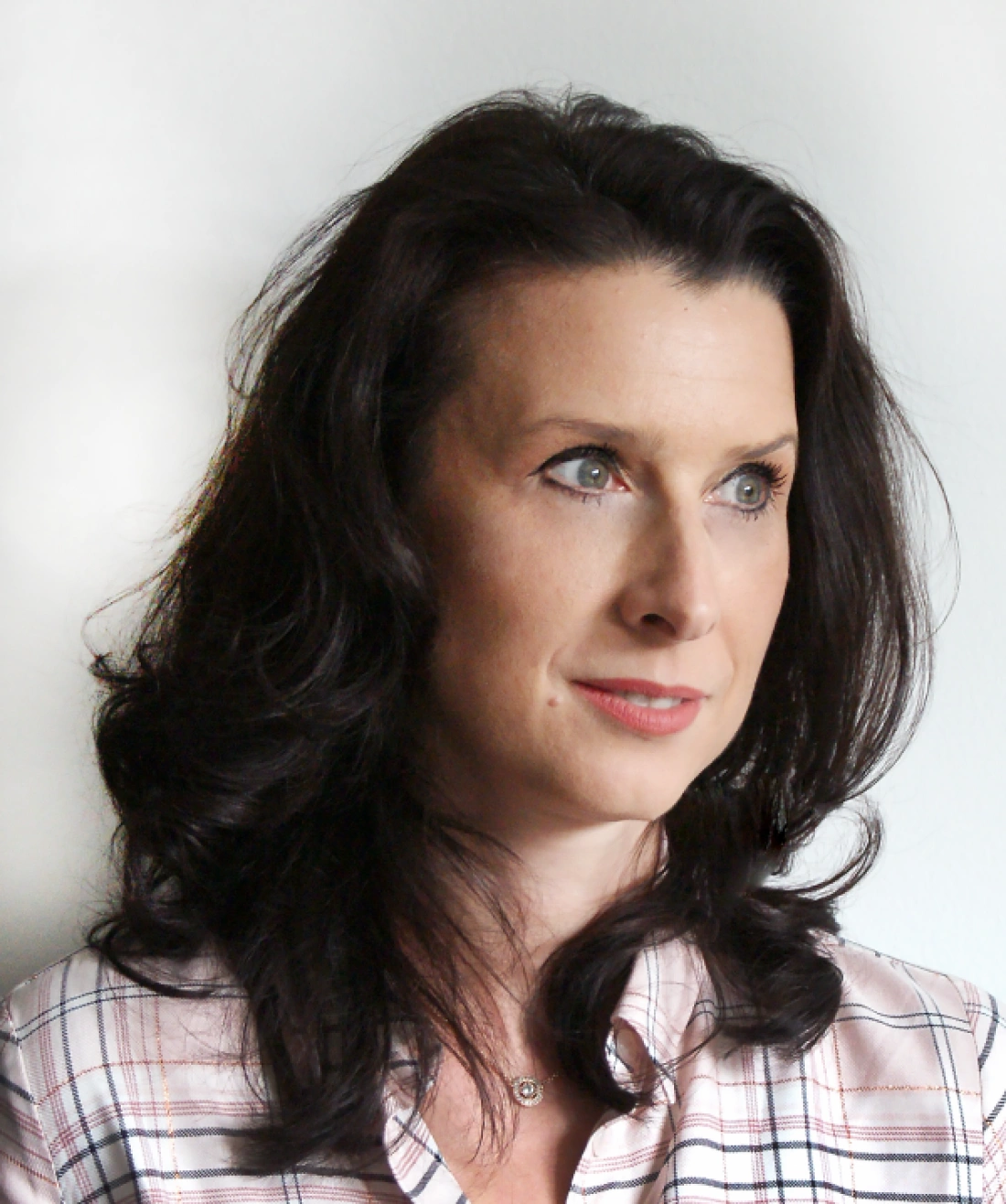 Portret kobiety o ciemnych włosach, z delikatnym uśmiechem, ubranej w koszulę w kratę.