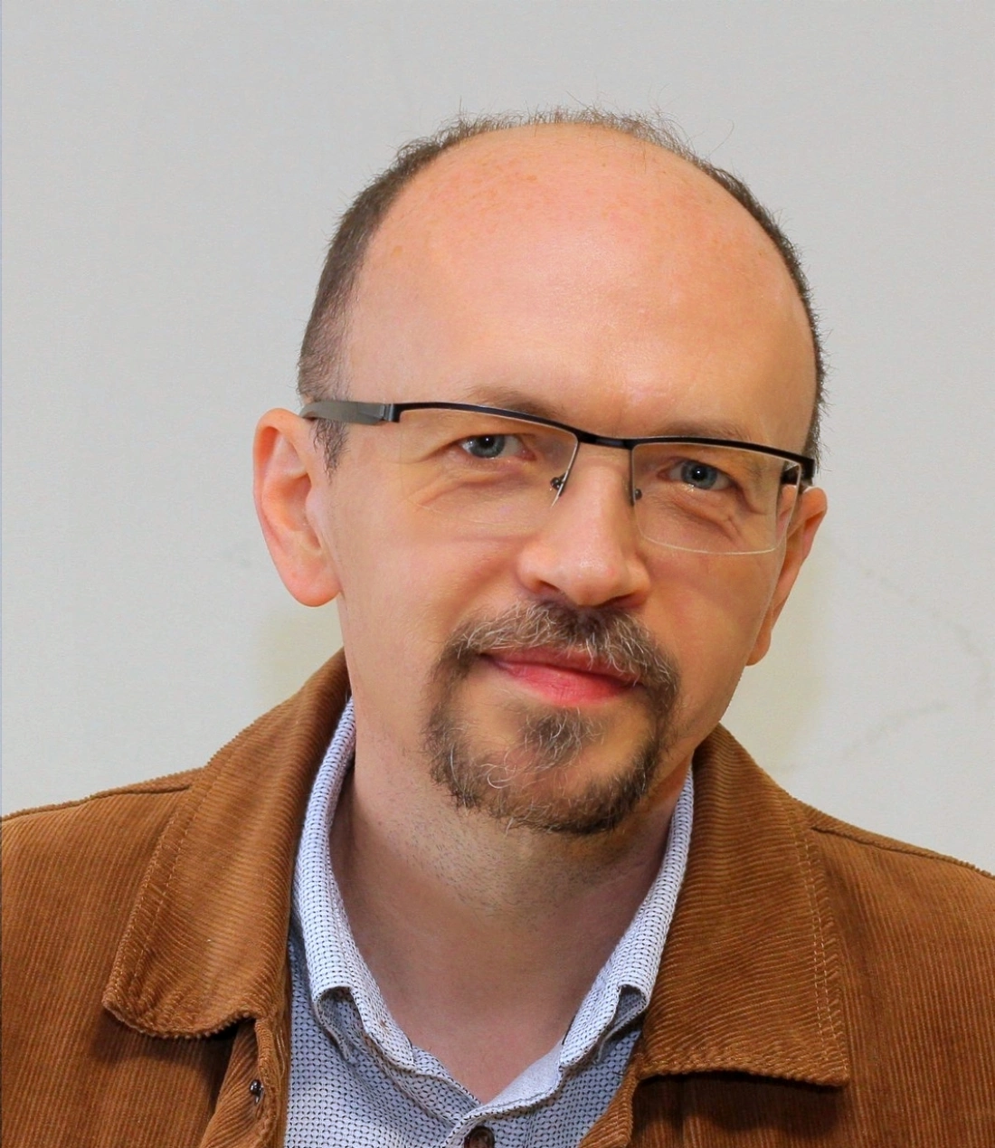 Mężczyzna w okularach z lekko zarostem, ubrany w brązową kamizelkę.