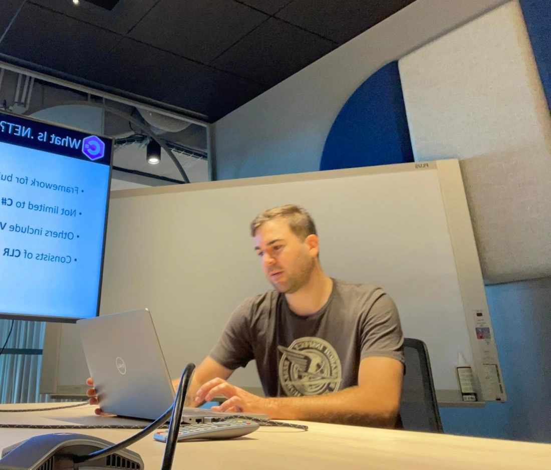 Mężczyzna pracuje przy laptopie w biurze, z prezentacją wyświetlaną na ścianie.