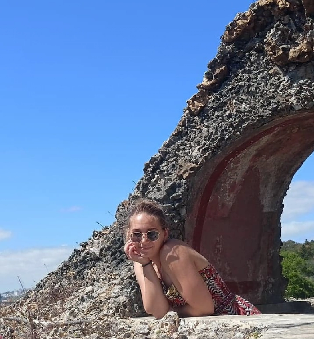 Młoda kobieta w okularach przeciwsłonecznych opiera się na ruinach w słoneczny dzień.