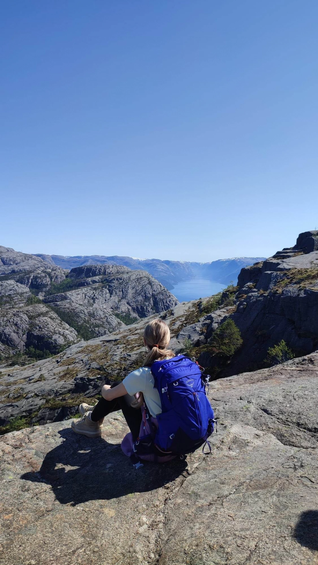 Osoba z plecakiem siedząca na skale, podziwiająca górski krajobraz i jezioro w tle.