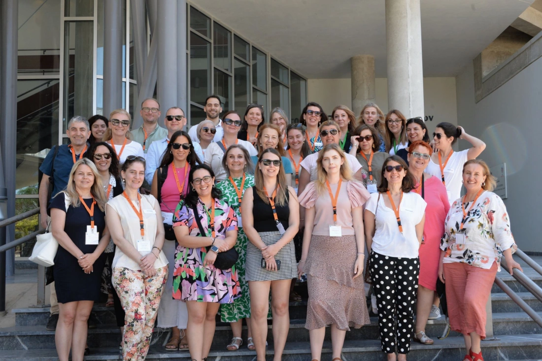 Kobieta z długimi, jasnymi włosami siedzi w pobliżu palm, spoglądając w dal na niebieskie niebo.