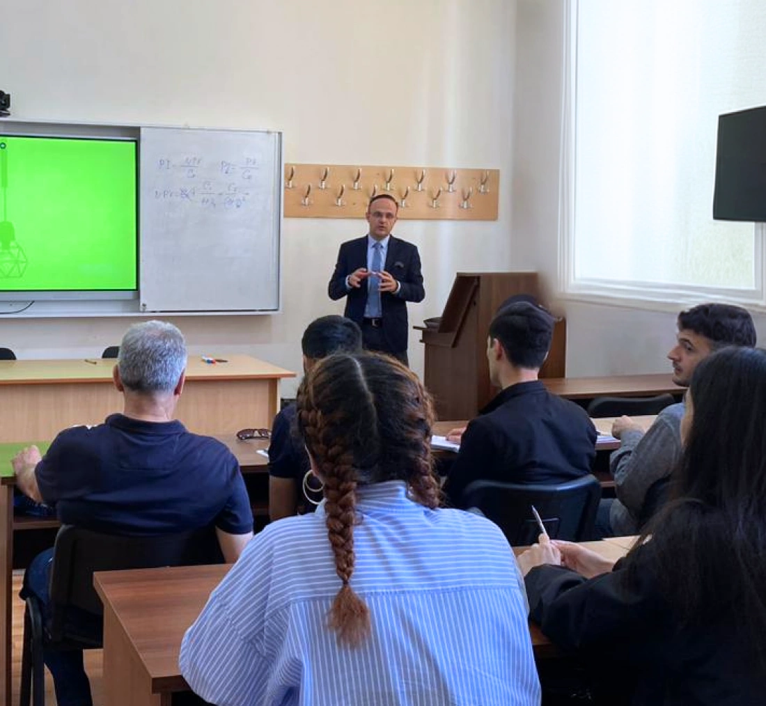 Wykład w klasie z nauczycielem prezentującym materiał na ekranie. Uczniowie w skupieniu słuchają.