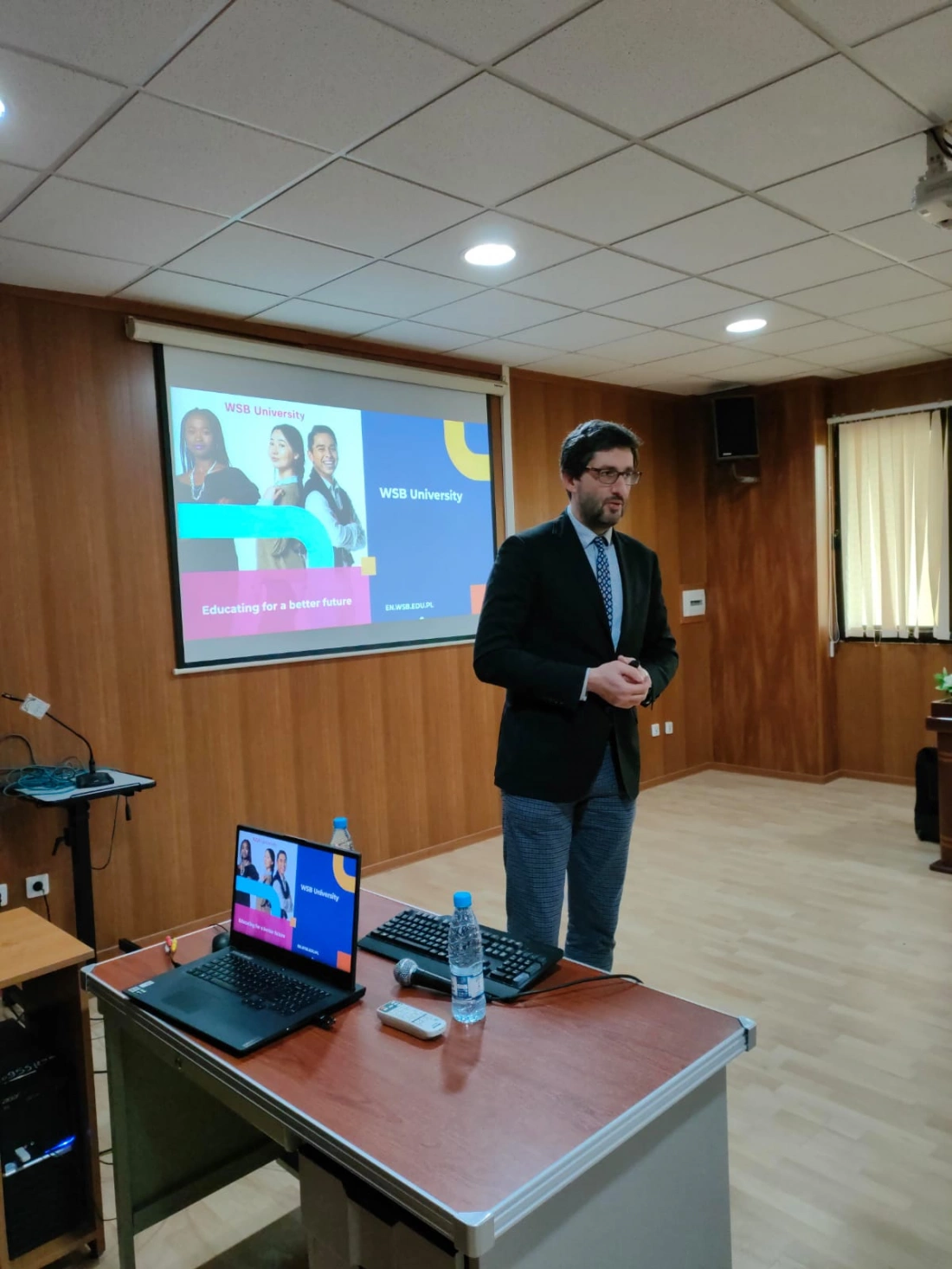 Mężczyzna prezentujący informacje o Uniwersytecie WSB na tle ekranu z grafiką.