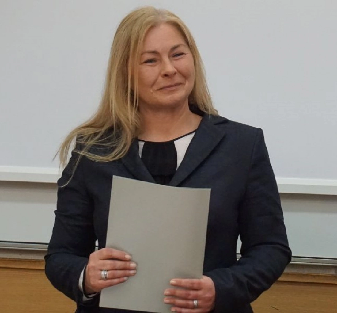 Kobieta w garniturze trzymająca dokumenty, uśmiechająca się.