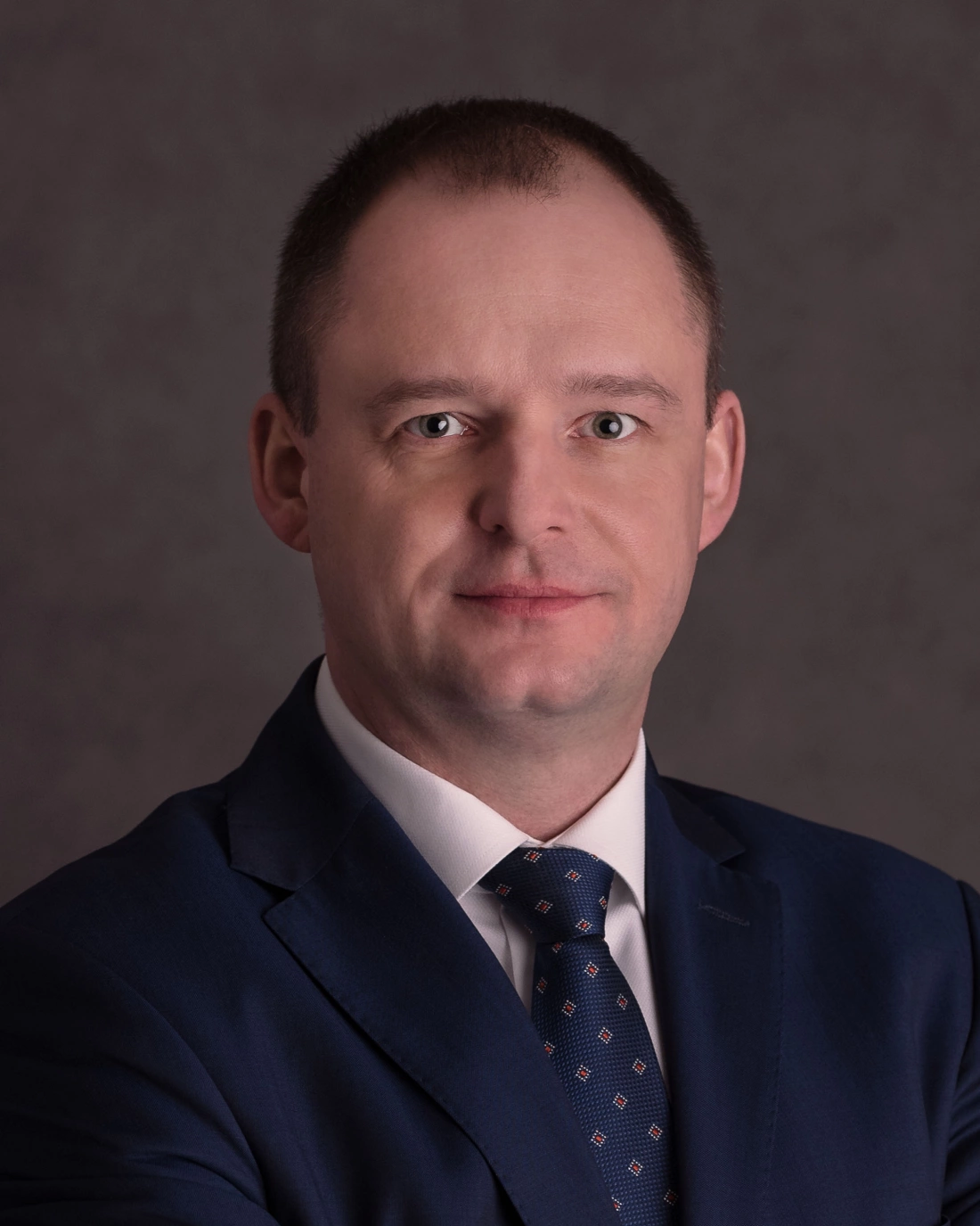 Mężczyzna w garniturze, uśmiechający się w profesjonalnym portrecie.