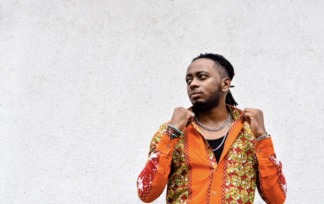 Mężczyzna w kolorowej koszuli z unikalnym wzorem stoi przed szarym tłem, z wyrazem twarzy pełnym pewności siebie.