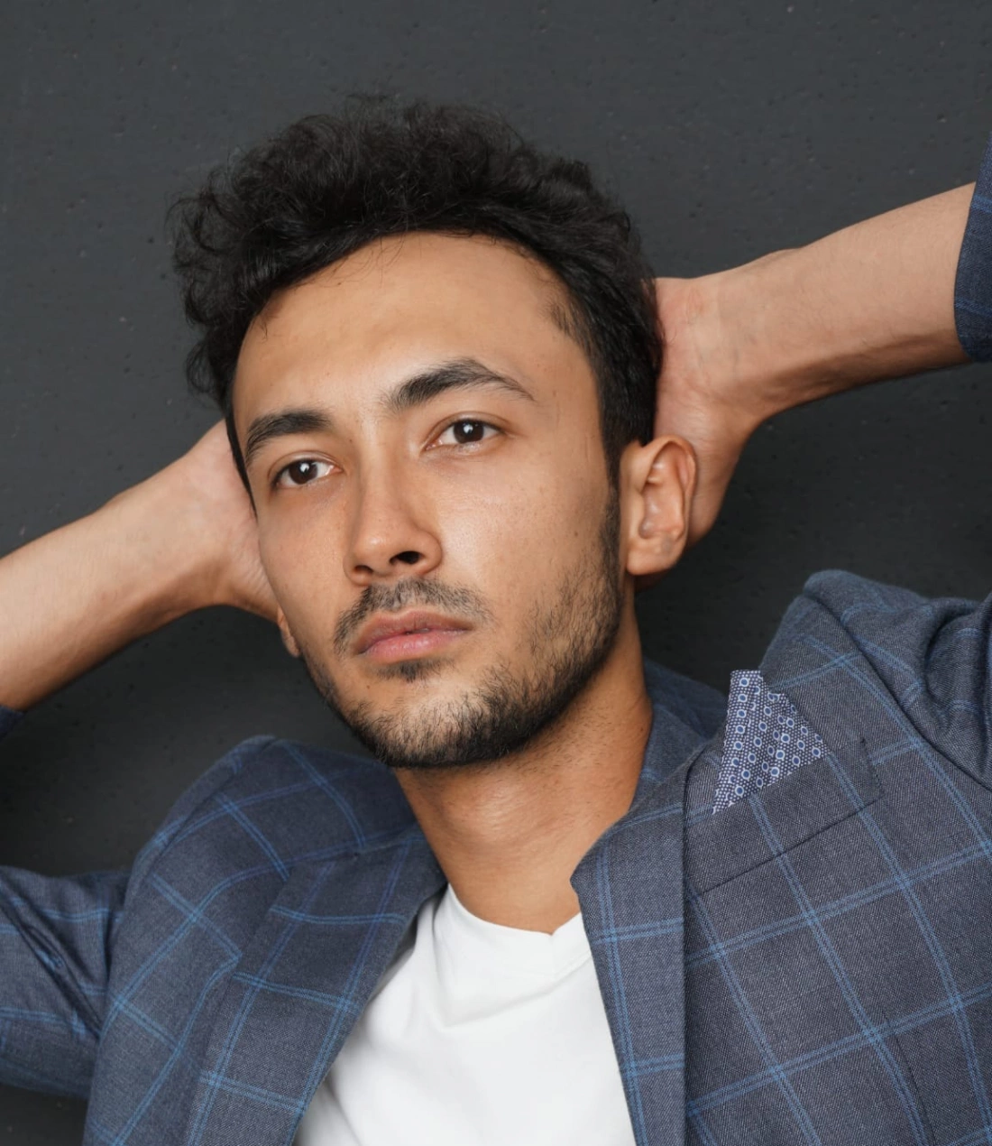 Mężczyzna w garniturze z wyrazem zamyślenia na tle szarej ściany.