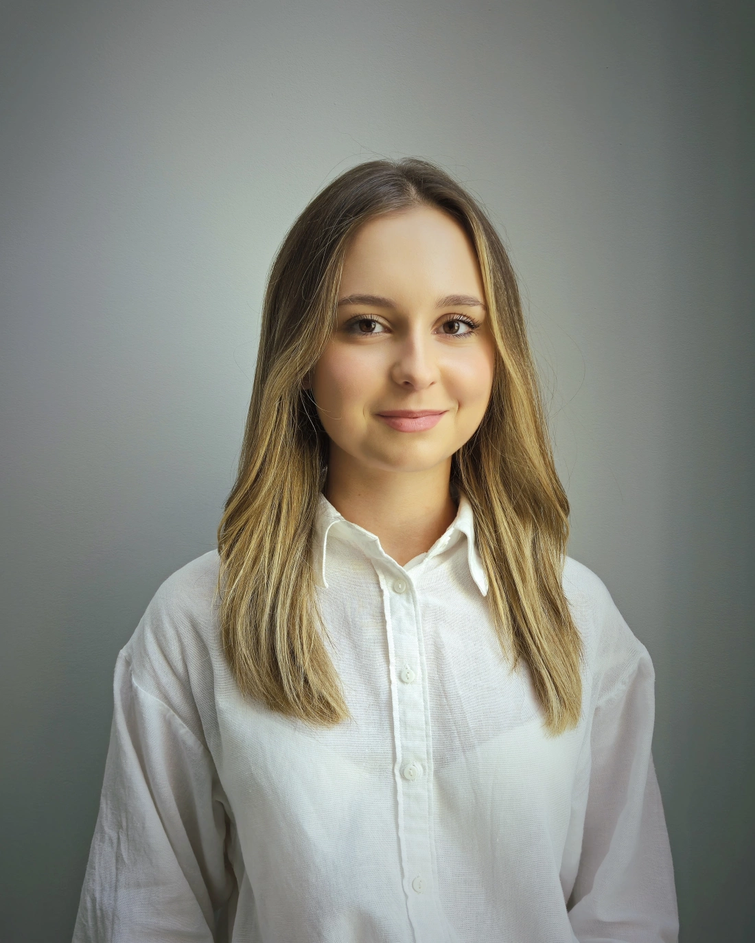 Kobieta z długimi, falującymi włosami i delikatnym makijażem, stoi na neutralnym tle.