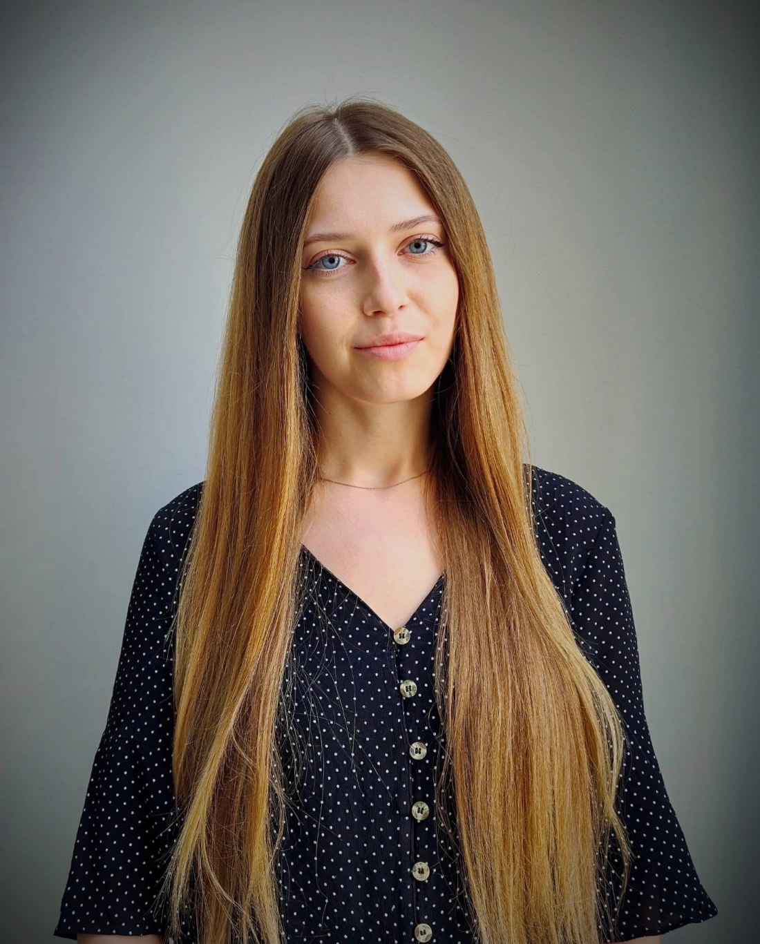 Portret młodej kobiety z długimi, prostymi włosami i niebieskimi oczami na jasnym tle.