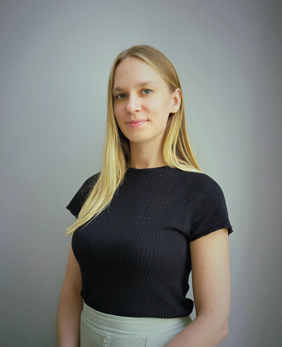 Portret młodej kobiety z długimi, prostymi włosami w jasnej bluzce, na tle ciemnoniebieskiej ściany.