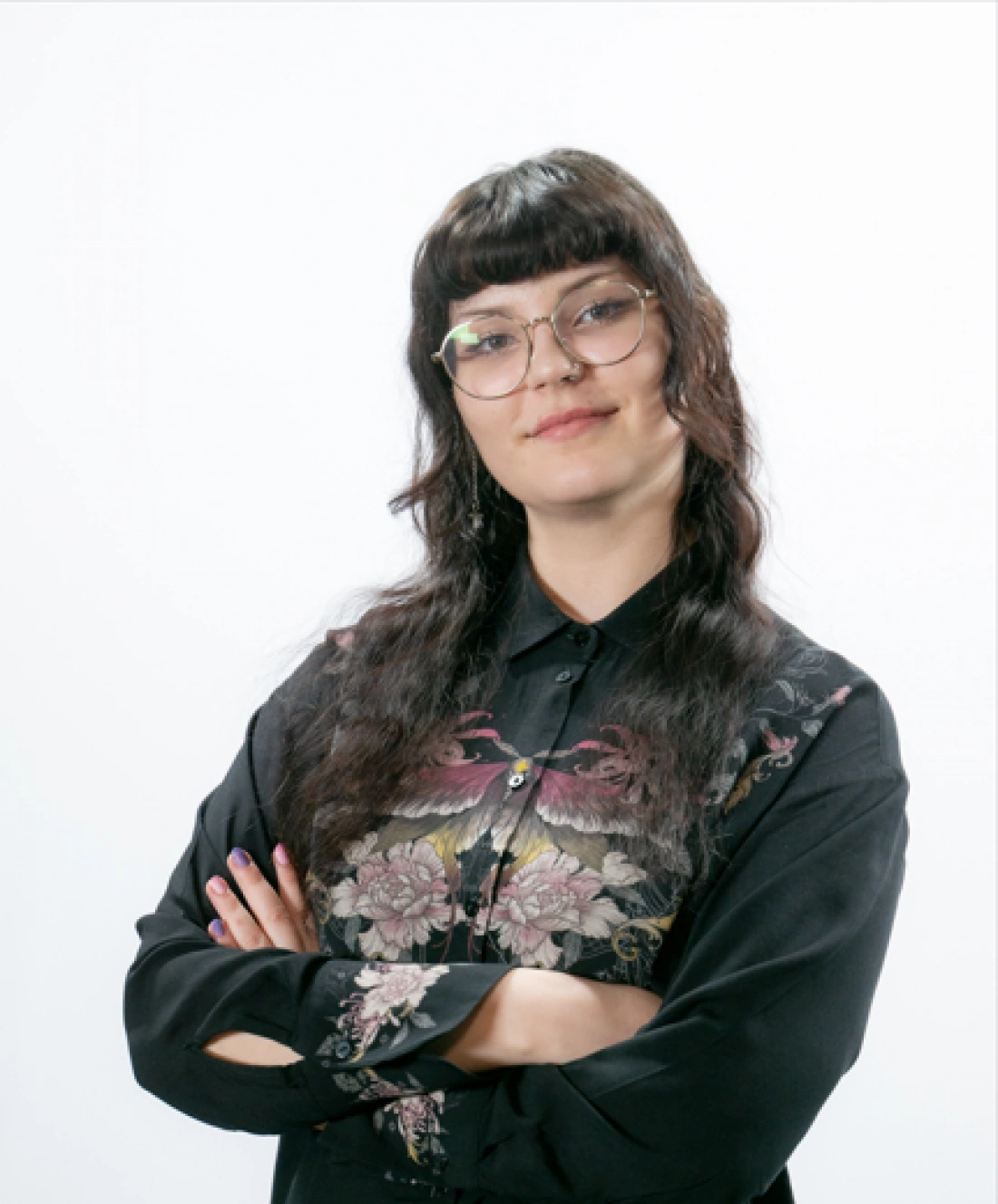 Młoda kobieta w fioletowym hijabie i białej koszuli, uśmiechająca się i trzymająca rękę przy twarzy.