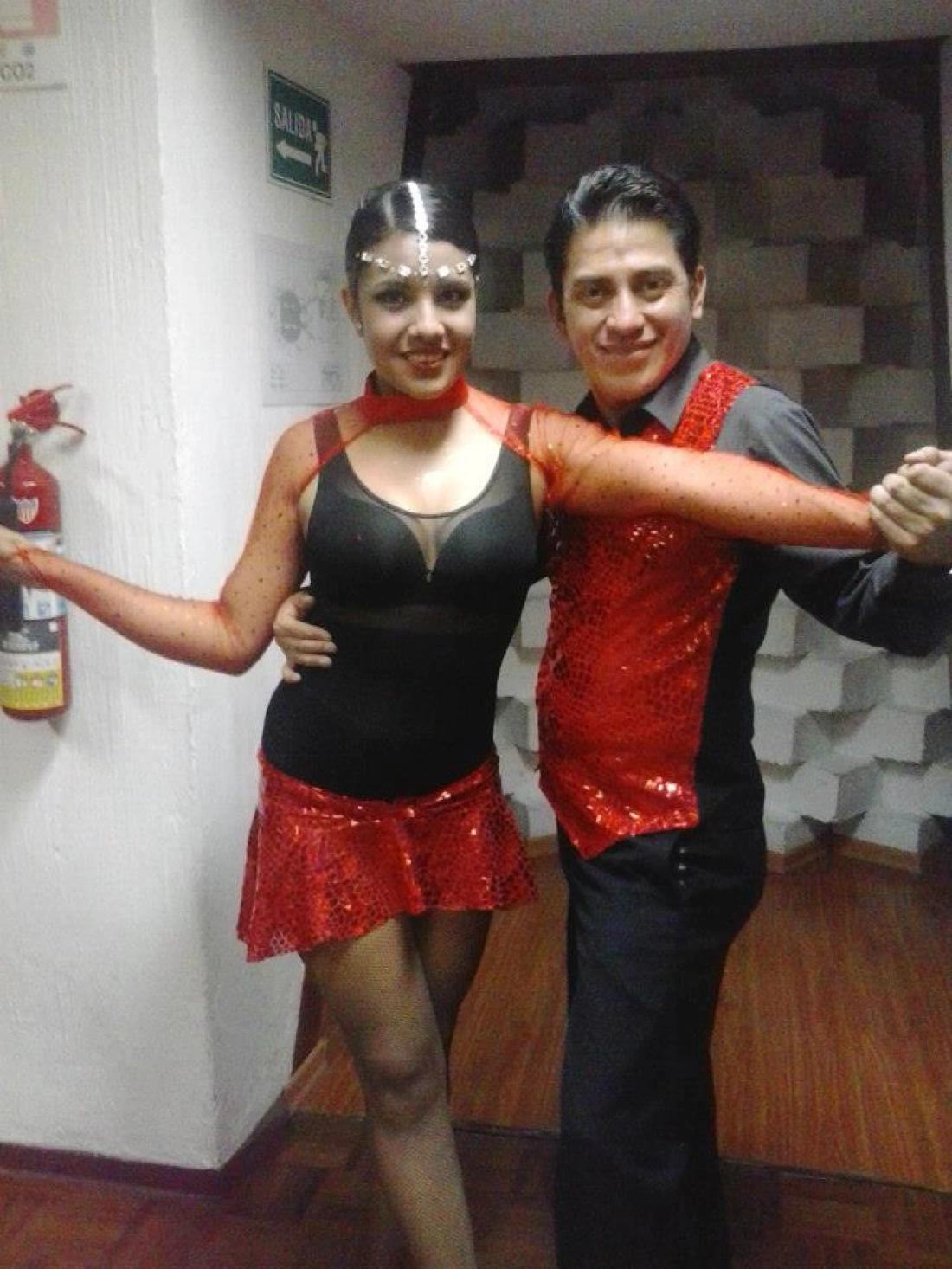 Para tańca w strojach w odcieniach czerwieni, z uśmiechem na twarzach.