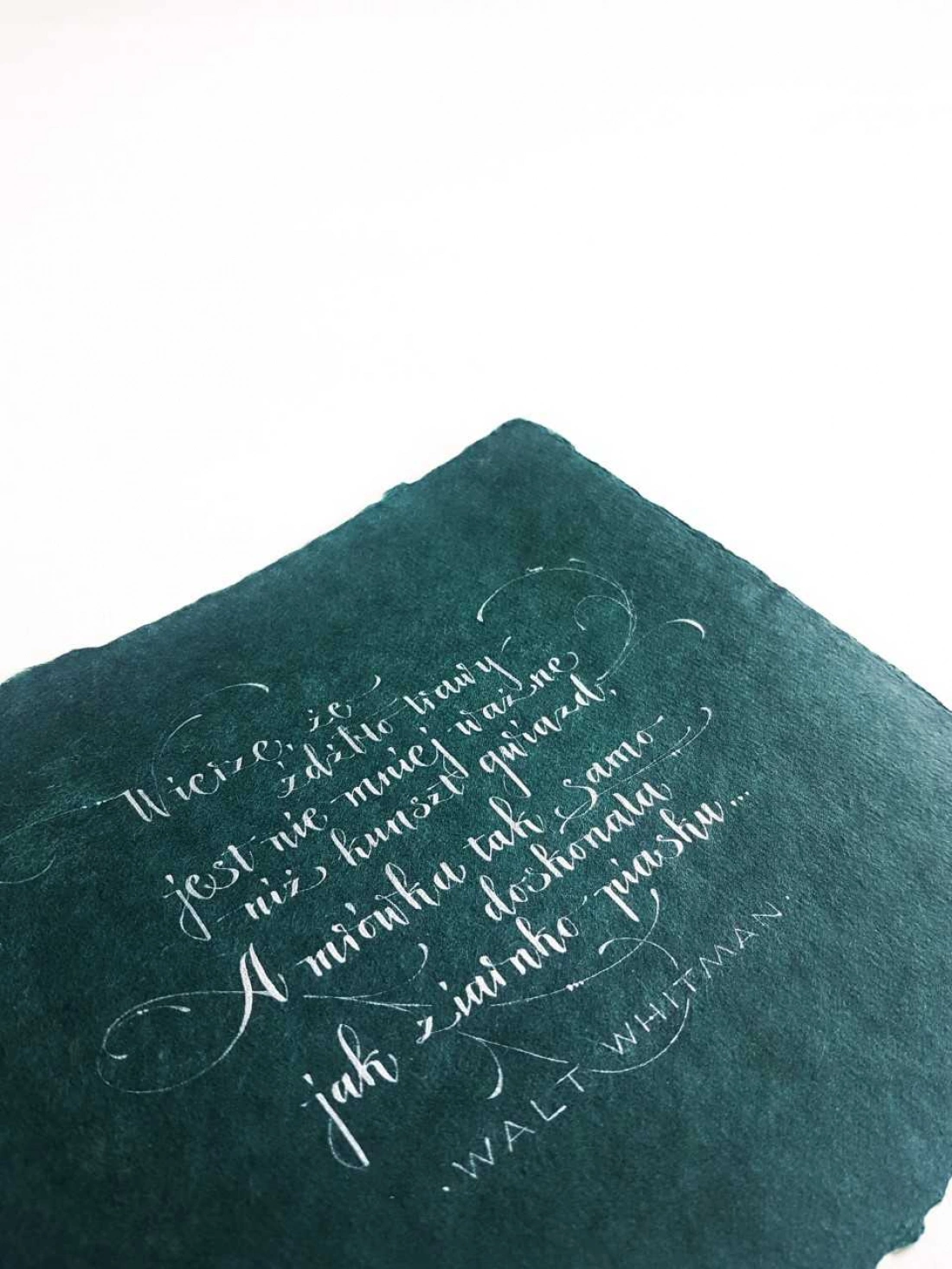 Zielony arkusz papieru z kaligrafowanym cytatem Walt'a Whitmana.