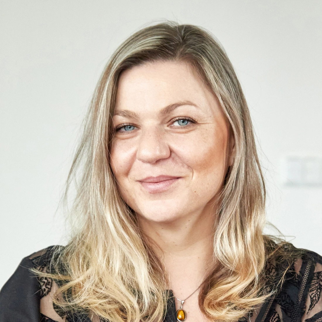 Portret uśmiechniętej kobiety z długimi, jasnymi włosami.